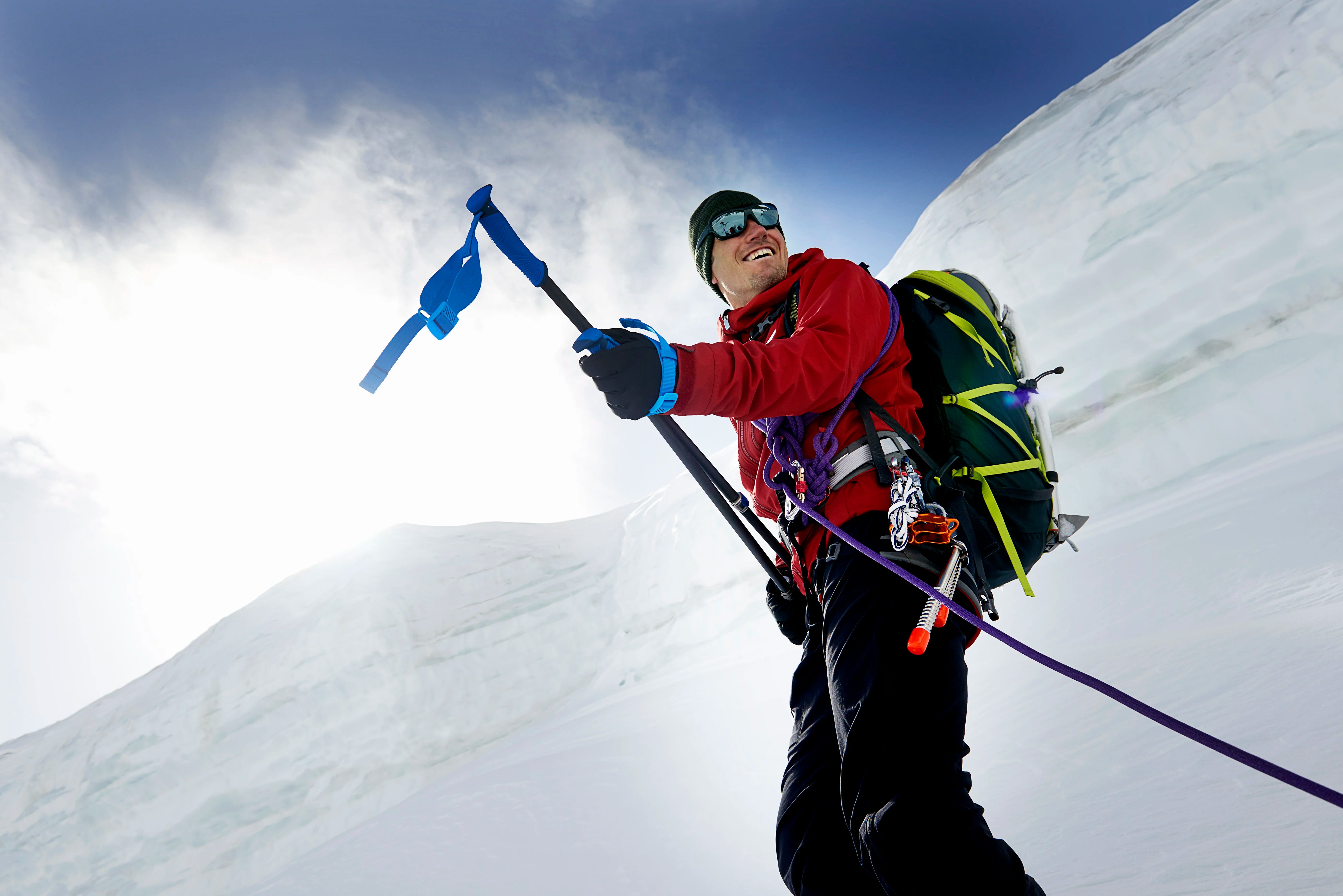 Alpiniste souriant équipé d’un piolet dans une pente enneigée, aventure en haute montagne.