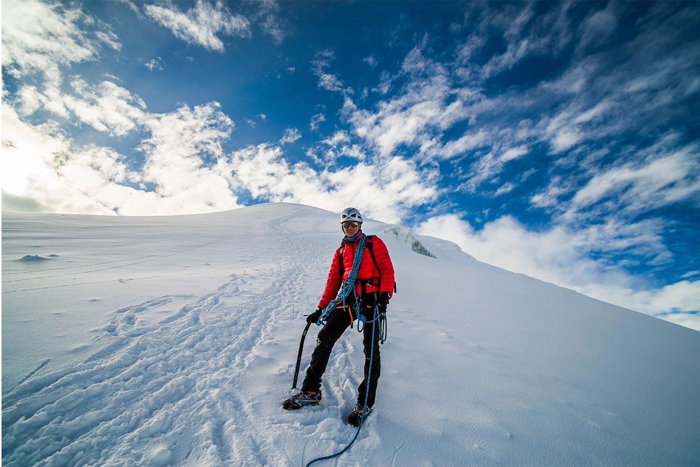 Alpiniste en doudoune rouge équipé d’un piolet lors d’une montée vers le sommet du Mont-Blanc sous un ciel dégagé.
