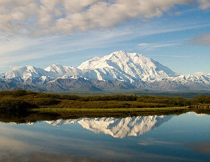 Vue du Denali en Alaska avec son sommet enneigé se reflétant dans un lac calme, paysage de montagne idéal pour les amateurs de trek.